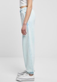 Svijetloplave trenirke s mekanom, glatkom teksturom, s elastičnim pojasom i manžetama na gležnjevima. Primjetan suptilan tie-dye uzorak.