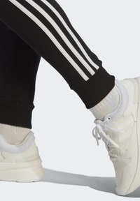 Svarta träningsbyxor med vita ränder längs sidan, ihopparat med vita sportskor med nät-detaljer och snören. Ribbad fotledsmansk.