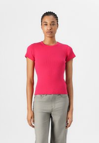 T-shirt ajusté à manches courtes en tissu côtelé rose vif. Encolure ronde, texture lisse, accompagné de pantalons gris clair.