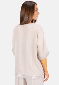 Hellbeige, locker sitzendes Oberteil aus strukturiertem Stoff, mit dezentem Glanz an den Bündchen und dem Saum. Schlichter runder Ausschnitt, weite Ärmel.