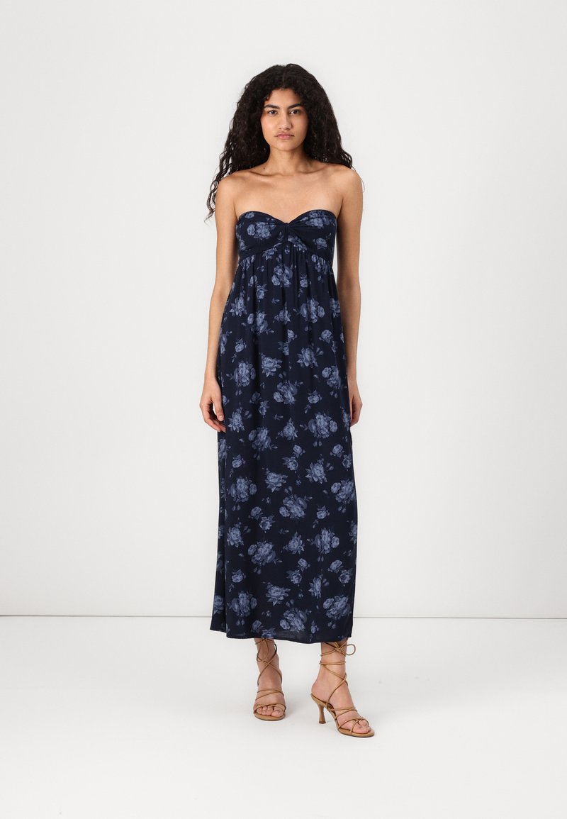 Marineblå blomster maxi-kjole med stroppeløs design, samlet kropp, og lett stoff. Har blå rose-mønstre og en løs passform.