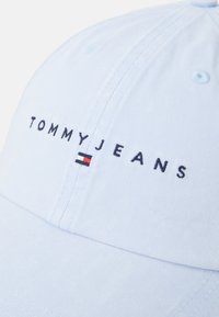 Lyseblå baseballcaps med brodert "TOMMY JEANS"-tekst i svart, med horisontale røde og hvite striper. Teksturiert stoff med synlige sømmer.