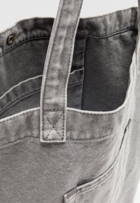 Sac fourre-tout en toile grise avec poignées cousues, fermeture par bouton pression, et poches visibles à l'intérieur et à l'extérieur.