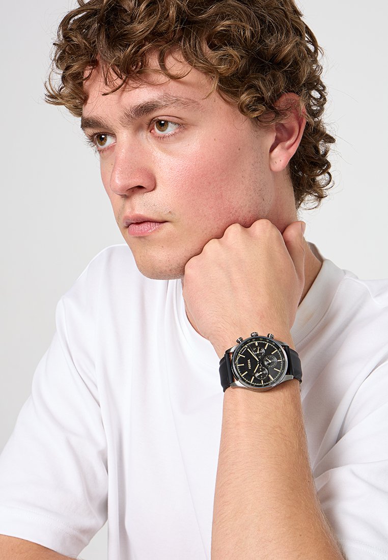 Orologio nero con cassa rotonda, accenti argentati e cinturino in gomma. L'orologio presenta quadranti cronografici e uno sfondo del quadrante testurizzato.