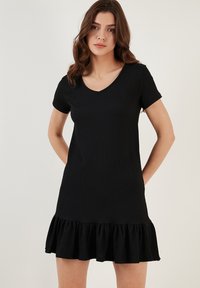 Black short-sleeve dress with a V-neck, featuring a textured fabric and a flared ruffle hem. Simple, casual design suitable for various occasions.