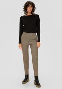 Zwarte lange mouw top gecombineerd met bruine broek met houndstoothpatroon. De broek heeft een getailleerd ontwerp en knoopsluiting. Zwarte chunky laarzen.