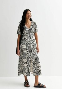 Vestido midi de estampado floral en blanco y negro con mangas abullonadas y escote en V. Cuenta con botones en la parte delantera y una falda fluida. Llevado con sandalias negras.