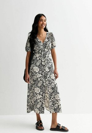 Black and white floral print midi dress with puff sleeves and a V-neck. Features a button-front and flowing skirt. Worn with black sandals.