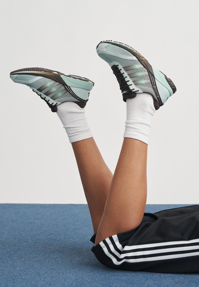 Ljusblå och svarta sportskor i mesh-material, med tre mörka ränder på sidan och texturerade sulor; matchade med vita strumpor.