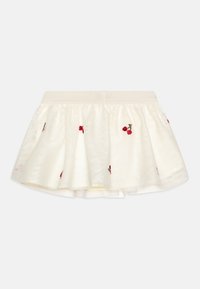 Jupe blanche à plusieurs couches avec des broderies de cerises rouges. Elle présente une taille douce et une couche extérieure transparente avec une doublure intérieure lisse.