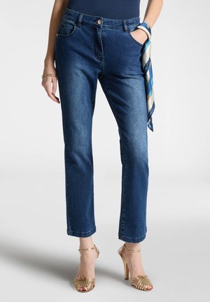 Jeans in denim blu scuro con cinque tasche, chiusura con bottone e design a gamba dritta. Indossati con scarpe con tacco a strappo dorate e una sciarpa fantasia.