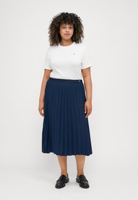 White crew-neck t-shirt paired with a navy pleated midi skirt. The skirt features a wide waistband and is made of lightweight fabric. Black loafers complete the outfit.