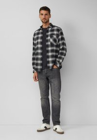 Schwarz-weiß karierte Flanellhemd über einem dunklen T-Shirt, kombiniert mit dunklen Jeans und weißen Sneakers. Verfügt über einen Knopfverschluss und eine Tasche.