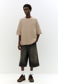 Béžový pletený nadmerný top s krátkym rukávom, spárovaný s tmavomodrými denimovými culottes. Hnedé a čierne tenisky, biele ponožky. Jednoduchý dizajn s voľným strihom.