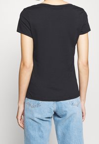 Black short-sleeve t-shirt in soft fabric, featuring a round neckline and a slim fit, paired with light blue jeans. Minimalist design.