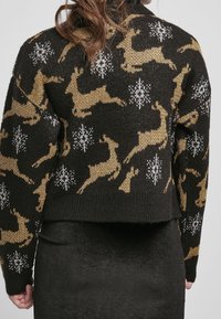 Pull en tricot noir avec des motifs de rennes dorés et de flocons de neige blancs. Design cropped, tissu texturé et ourlet côtelé.