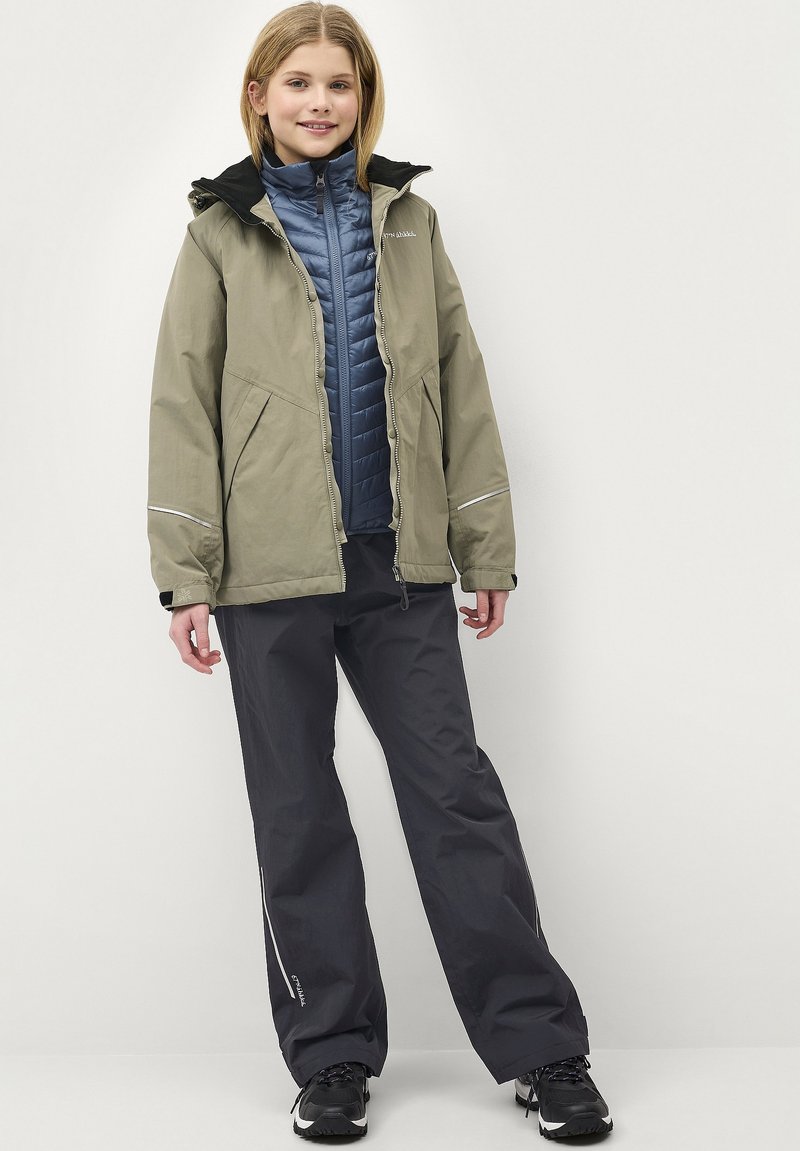 Olivengroene buitenjas met zwarte capuchon, blauwe geïsoleerde binnenvest, grijze broek en zwarte schoenen. Bevat reflecterende accenten en ritsen.