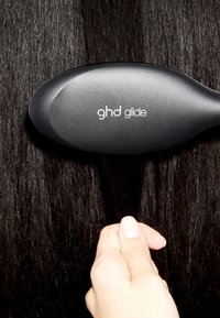 Hand houdt een gedeelte van het donkere haar vast terwijl het met een zwarte ghd glide haarborstel door het rechte zwarte haar gaat.
