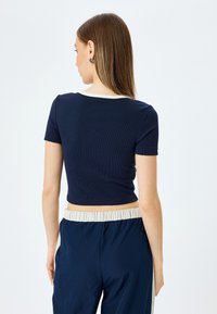 Top corto acanalado azul marino con mangas cortas y un cuello crema, combinado con pantalones fluidos azul marino con una cinturilla elástica.