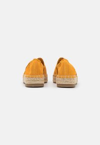 Dzelteni espadrilles ar mīkstu zamšu augšdaļu un austām jutu zolēm, ar slip-on dizainu un noapaļotu purngala daļu.