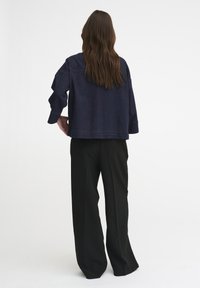 Giacca di jeans scura con vestibilità ampia, spalle scese e maniche lunghe, abbinata a pantaloni neri a gamba larga a vita alta.