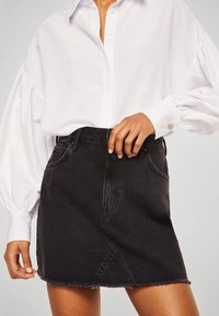 Blusa blanca con mangas abullonadas, combinada con una minifalda de mezclilla negra que presenta un dobladillo deshilachado y un detalle de costura diagonal.