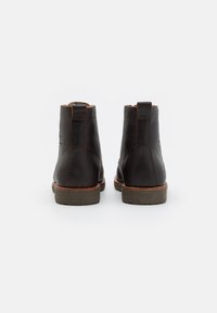 Botas de tobillo de cuero marrón con un acabado suave, punta redonda y suela contrastante. Presenta pequeños lazos para facilitar el uso.