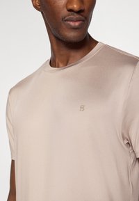 Μπεζ κοντομάνικη μπλούζα κατασκευασμένη από απαλό, ελαφρύ ύφασμα. Διαθέτει απλό, ανάγλυφο λογότυπο στην αριστερή πλευρά του στήθους.