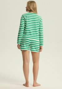 Zielono-biała paskowana bluzka z długim rękawem w połączeniu z pasującymi szortami, wykonana z miękkiego materiału. Krótkie rękawy, luźny krój oraz minimalne akcenty.