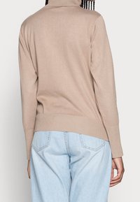 Pull à col roulé en tricot beige avec texture côtelée et manches longues. Assorti à un jean taille haute bleu clair.