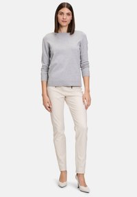 Grauer Strickpullover mit Rundhalsausschnitt, langen Ärmeln, kombiniert mit beigen Slim-Fit-Hosen und weißen High Heels. Einfaches Design und weicher Stoff.