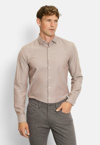 Hellebraunes Langarmhemd mit Button-Down-Kragen, das eine feine Textur und weiße Knöpfe aufweist, kombiniert mit dunklen gemusterten Hosen.