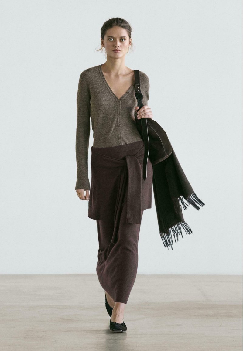 Brauner Strickcardigan mit Knopfdetail, kombiniert mit einem braunen Wickelrock. Akzentuiert mit einem dunklen Schal und einer schwarzen Tasche.