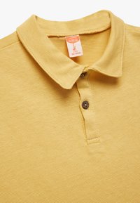 Polo de algodón de un suave y texturizado color mostaza, con cuello, cierre de dos botones y detalle de etiqueta tejida. Apto para edades de 4 a 5 años.