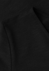 Gros plan sur un tissu noir montrant une texture tricotée pliée et une couture fine le long du bord.
