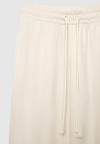 Joggers beige clair avec taille élastique et cordon de serrage, fabriqués en tissu doux. Finition avec des accents en forme de pampilles sur le cordon.