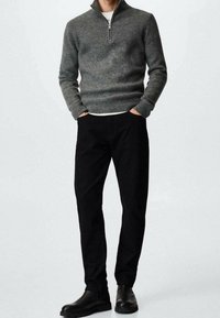 Grau gestrickter Pullover mit einem Viertelreißverschluss-Kragen, kombiniert mit schwarzen Hosen. Die Person trägt schwarze Stiefeletten. Einfaches, modernes Design.