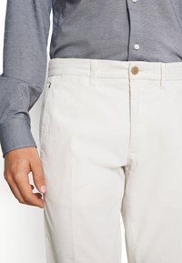 Pantalones de pana blancos con cierre de botón y bolsillos laterales, combinados con una camisa de botones azul oscura con una tela texturizada.