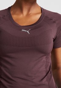 Viininpunainen urheilupaita teksturoiduilla paneeleilla, lyhyillä hihoilla ja pyöreällä kaula-aukolla. Rintakehässä heijastava Puma-logo.