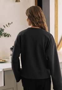 Schwarzer übergroßer Sweatshirt mit Rundhalsausschnitt, überschnittenen Schultern und geradem Saum. Weiche Stoffstruktur, von hinten betrachtet.