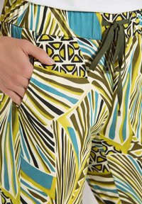 Gemusterte Hose mit einem lebhaften Design in grün, blau und schwarzen Linien. Mit elastischem Bund und Taschen. Aus leichtem Stoff gefertigt.