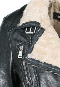 Zwarte leren jas met een crèmekleurige faux shearling kraag, zilveren hardware, ritszakken en een gestructureerde afwerking. Kenmerkende gespdetails.