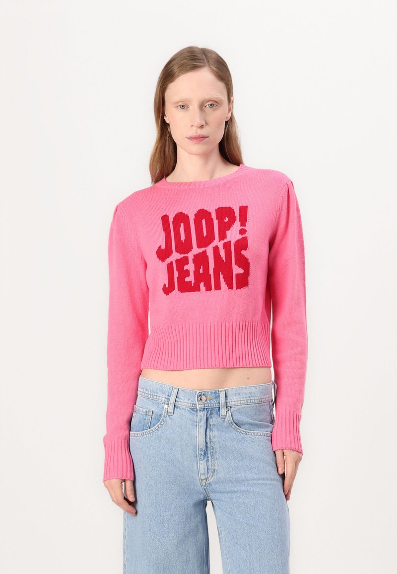 Roza skraćena jakna s rebrastom teksturom i crvenim grafičkim natpisom "JOOP! JEANS" sprijeda, uparena s svijetloplavim trapericama.