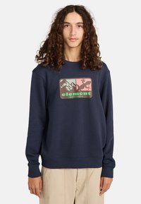 Granatowy sweatshirt o miękkiej teksturze, z prostokątną grafiką przedstawiającą góry i jaszczurkę, akcentowany zielonymi i różowymi kolorami.