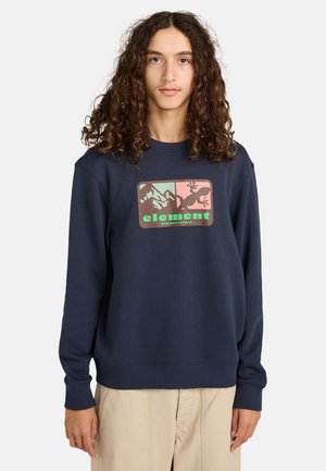 Sweatshirt bleu marine en texture douce, présentant un graphique rectangulaire avec des montagnes et un lézard, accentué de couleurs vertes et roses.