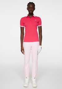 Rosa piké med vit krage och randiga ärmar, i kombination med ljusrosa byxor. Vit golfhandske på vänster hand och vita sneakers.