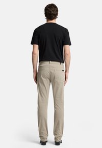 Beiga bomullbyxor med slim fit, utrustade med bakfickor och en svart etikett, kombinerade med en svart t-shirt med kort ärm.