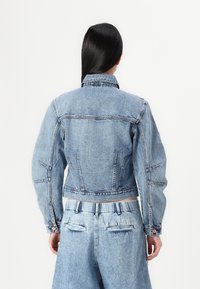 Denim jakna svijetlo plave boje, s krojenjem do struka, šiljastim kragnom i prednjim džepovima. Vidljivi detalji šivanja i dugmad.
