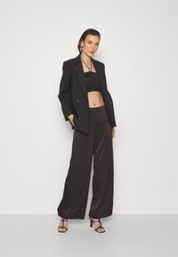 Svart blazer over en svart rynket crop topp og vide satinsbukser. Tilbehør inkluderer store hoop-øreringer og remsandaler med høy hæl.