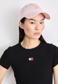 Cappellino da baseball rosa chiaro con logo ricamato, abbinato a una t-shirt nera aderente con una piccola patch colorata "Tommy Jeans".